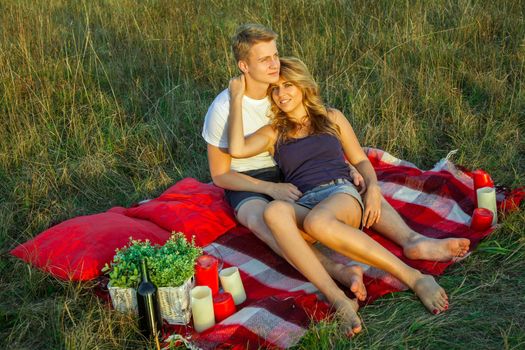 Beautiful young happy loving couple on picnic lying down on plaid in field on sunny summer day enjoying and resting. looking at camera and smiling. top view.