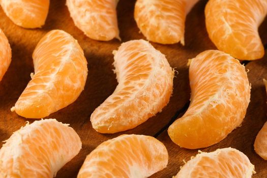 Fresh satsuma mandarin tangerine (Citrus unshiu) fruit wedge layout on natural wood surface abstract, South Africa