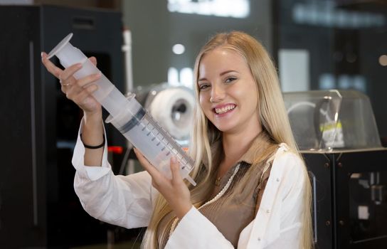 Young smiling woman analyzing machine part during her scientific experiment in laboratory.