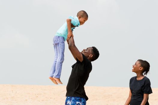 young man raising his little brother and little sister looks at them smiling.