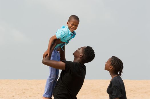 young man raising his little brother and little sister looks at them smiling.