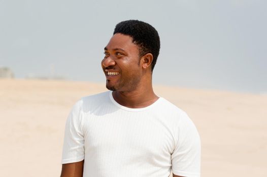 portrait of young man in white t-shirt standing and smiling at the beach.