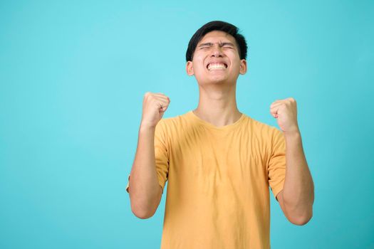 Young man over blue background very happy and excited doing winner gesture with arms raised, smiling and screaming for success. Celebration.