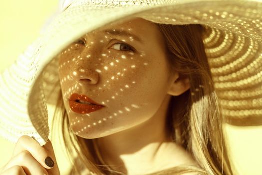 Fashion beauty portrait of a woman in a hat, a shadow falls on a woman from a hat and looking at camera. Yellow background, outdoor
