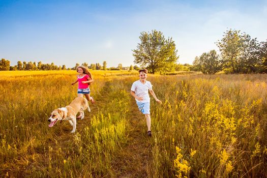 Brother and sister runs in a green field with their beautiful Alabai pet dog.