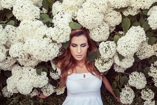 Beautiful woman closed eyes, posing near white flowers. Outdoor spring or summer photo