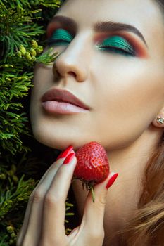 Portrait of woman with perfect skin and makeup, holding near face red sweet strawberry. Outdoor spring or summer photo