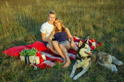Beautiful young happy loving couple on picnic lying down on plaid with their dog in field on sunny summer day enjoying and resting. looking at camera and smiling. top view.