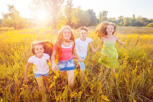 four happy beautiful children running playing moving together in the beautiful summer day. jumping and looking at camera with happiness and toothy smile.