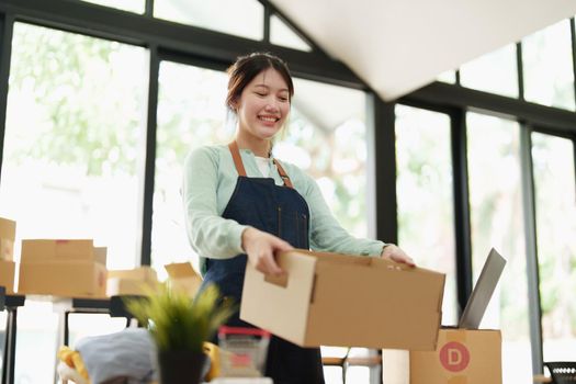 Portrait of a small startup Asian female entrepreneur SME owner picking up a yellow shirt before packing it in an inner box with a customer. Online Business Ideas and Freelance.