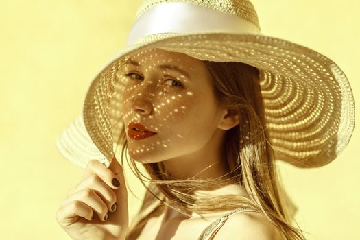 Attractive cheerful woman portrait in summer. Beautiful freckled girl in straw hat. Looking at camera. Isolated on yellow background in studio shot