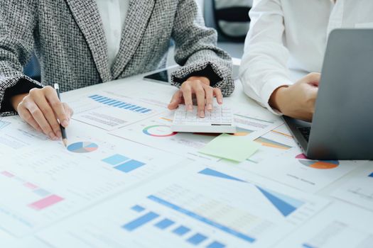 two young Asian businesswoman using their tablet computers with documents and calculator to plan marketing strategies and investments to profit from their clients.