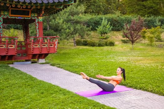 Cheerful young beautiful woman practicing and posing yoga in the east Asian park.