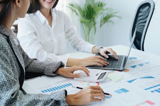 two young Asian businesswoman using their tablet computers with calculators and documents to plan marketing strategies and investments to profit from their clients.