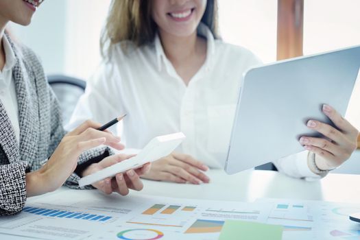 two young Asian businesswoman using their tablet computers with calculators and documents to plan marketing strategies and investments to profit from their clients.