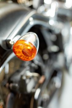 Closeup rear view of a taillight on a motorbike. Orange turning light on a blurred black vintage motorcycle. One modern chrome transportation vehicle. Maintenance on a shiny classic retro custom bike.