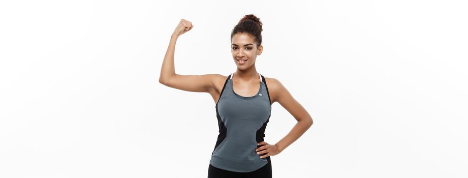 Healthy and Fitness concept - Portrait of young beautiful African American showing her strong muscle with confident cheerful facial expression. Isolated on white studio background