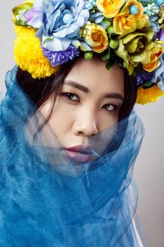 portrait of sensual asian beautiful woman with floral hat and blue veil on light grey background, closeup . indoor studio shot.