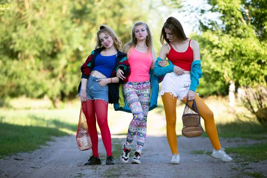 Three beautiful country girls dressed in the style of the nineties are walking along the road.