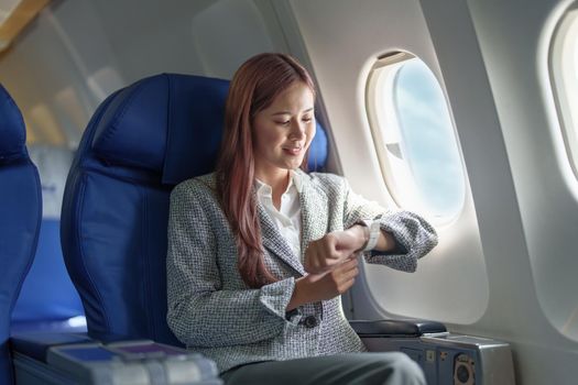 Portrait of a smiling Asian businesswoman looking at the time on the plane.