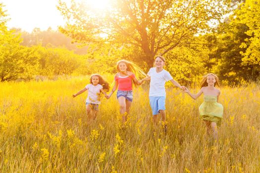 four happy beautiful children running playing moving together in the beautiful summer day. jumping and looking at camera with happiness and toothy smile.