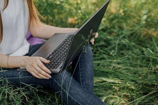 girl sits on the grass and works at a laptop. freelance