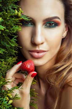 Handsome model with perfect green makeup looking at camera and holding red berry. Outdoor spring or summer photo