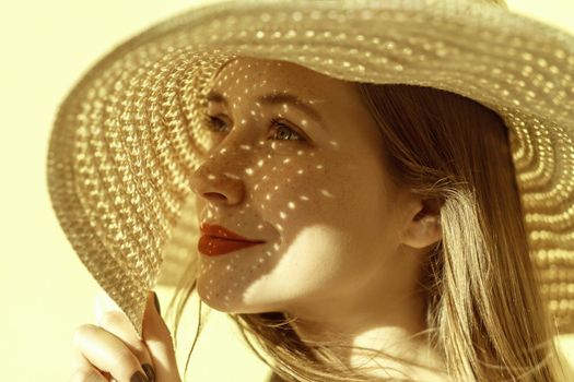 Lady in straw hat in summer. Closeup, portrait of a beautiful and happy freckled woman. Indoor, studio shot. Yellow background
