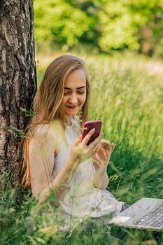 girl sitting on the grass looking at the phone. freelance. selfeducation. the concept of remote learning and outdoor work