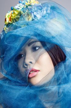 portrait of asian woman with floral hat and blue veil looking aside on light grey background . indoor studio shot.