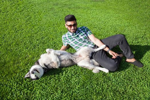 Young man sitting at green lawn and enjoying with his dog