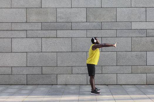 Afro american man in yellow sportswear stretching before doing morning workout. Young African jogger warming up before outdoor run