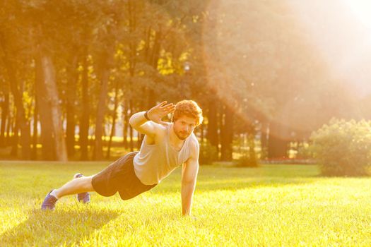 Training in one summer morning. Young adult bearded man looking in camera and doing exercise. Outdoor