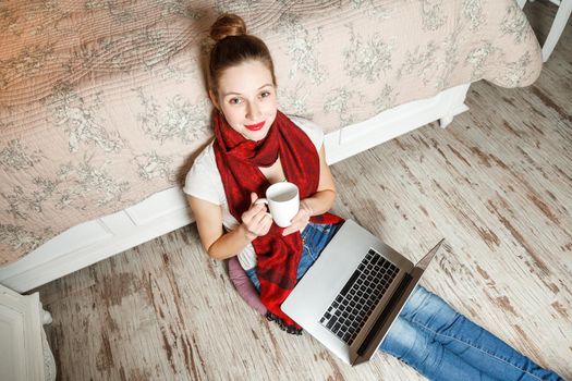 Happy beautiful girl with laptop and coffee sitting and resting on floor and working with laptop.