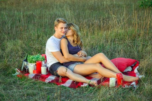 Beautiful young happy loving couple on picnic lying down on plaid on sunny summer day enjoying and resting. hugging and she is kissing her love.