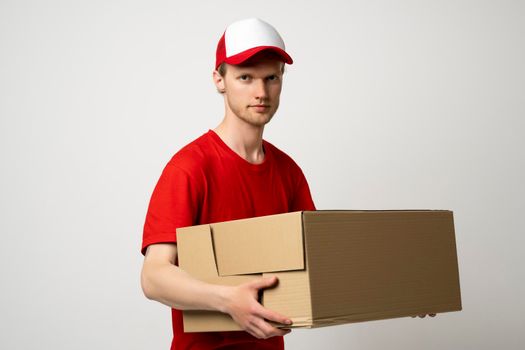 Courier man in a red uniform holding a cardboard box. Parcels Delivery Service Concept