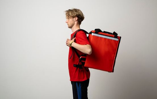 Young courier in red t-shirt with a red thermo bag on white background. Food delivery service