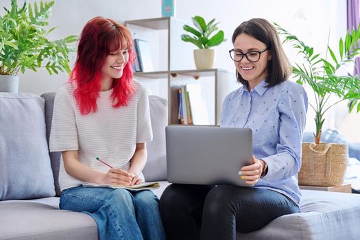 Female teacher teaches student teenage girl, sitting together on couch in office, educational counseling, using laptop. Education, knowledge, individual training, adolescence concept