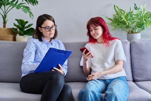 Psychologist counseling teenage female, individual therapy in doctors office. Professional cocellor helping teenager, girl with smartphone. Mental health, adolescence, psychology, psychiatry concept