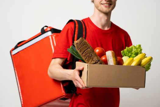 Food shipping, profession and people concept. Happy smiling delivery man with pepper box full of vegetables and thermal bag on a shoulder on white background