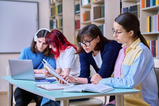 Group of teenage students study in school library classroom. Teen girl and female teacher mentor helping in their studies. High school, learning, education, knowledge, adolescence