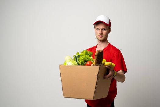 Food shipping, profession and people concept. Happy smiling delivery man with pepper box full of vegetables on white background