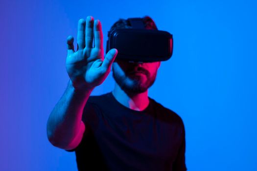 Young bearded man in virtual reality helmet plays online game in metaverse. Game simulates behavior in fictional world, gadgets and virtual reality addiction. Future technology concept