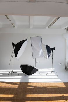 Professional lighting equipment, flashes, c-stands on a cyclorama in modern photo studio with a huge windows. Octabox, stripbox, softbox, buety plate and other stuff for photography