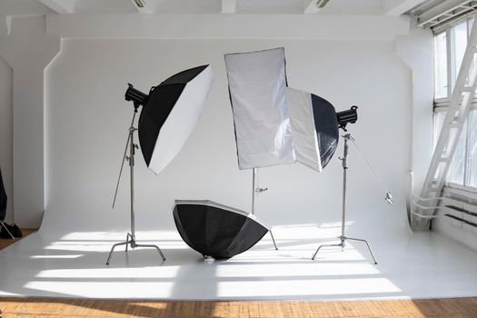 Professional lighting equipment, flashes, c-stands on a cyclorama in modern photo studio with a huge windows. Octabox, stripbox, softbox, buety plate and other stuff for photography