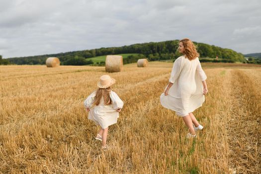 Mother plays with her daughter in a field with wheat