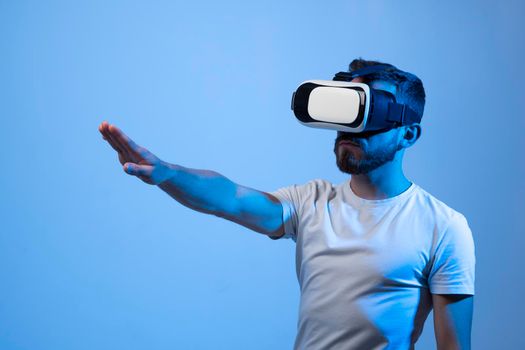 Young bearded man in virtual reality helmet plays online game in metaverse. Game simulates behavior in fictional world, gadgets and virtual reality addiction. Future technology concept