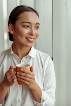 Portrait of asian business woman drinking coffee standing near windows at office. High quality photo
