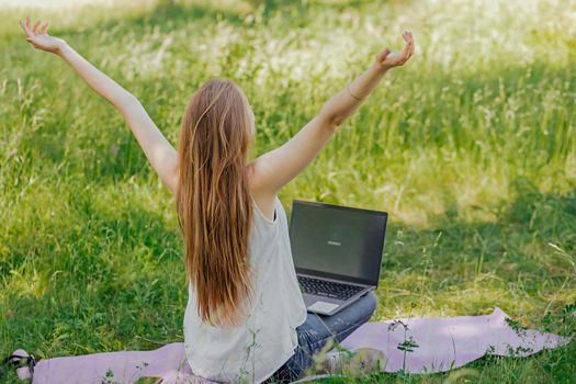 the girl sits outdoors and works at a laptop. she rejoices at the end of the working day. freelance. selfeducation. the concept of remote learning and outdoor work