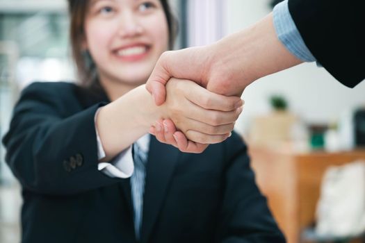 Unknown businesspeople are shaking their hands after signing a contract, while standing together in a sunny modern office, close-up. Business communication, handshake, and marketing concept.